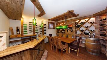 A rustic bar area with wooden furniture, a wine rack, and hanging green glass bottles.