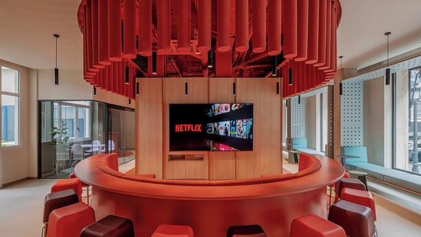 A modern bar area with a central Netflix screen, red seating, and large windows. - Residencia Universitaria Resa La Concepción (Valencia)