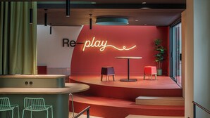 A modern interior with a stage, seating, and a neon sign reading "Re-play". - Residencia Universitaria Resa La Concepción (Valencia)
