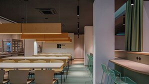 A modern dining area with long tables and chairs, a counter with stools, and pendant lighting. - Residencia Universitaria Resa La Concepción (Valencia)