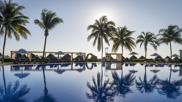 A pool with palm trees and umbrellas, surrounded by lounge chairs. - El Beso Adults Only at Ocean Coral & Turquesa - All inclusive (Puerto Morelos)