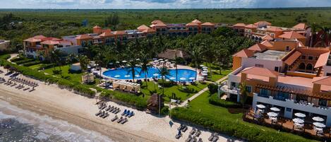 A resort with a large swimming pool, beach, and multiple buildings with red roofs.