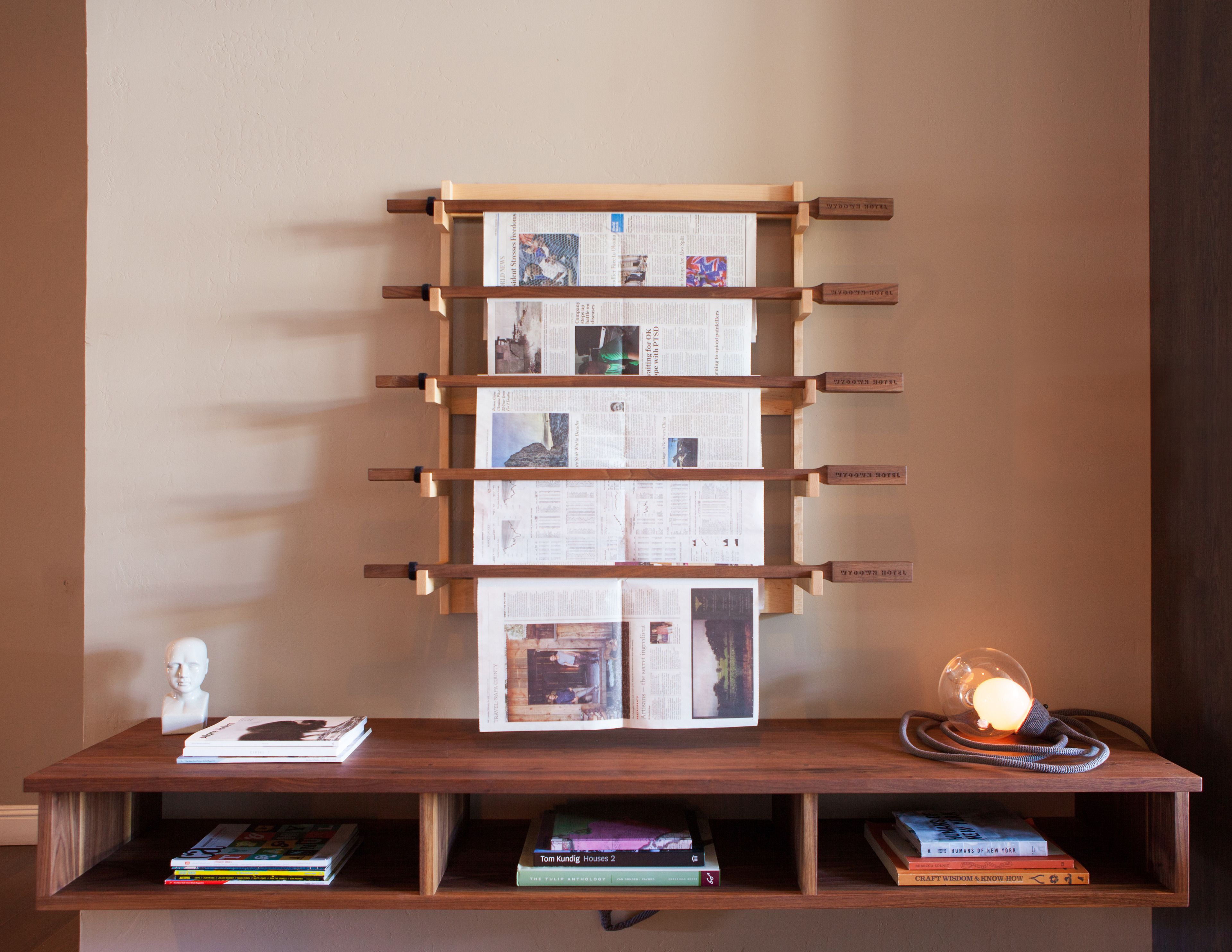 A wooden shelf with books and a bust, a wall-mounted display with papers, and a desk lamp.