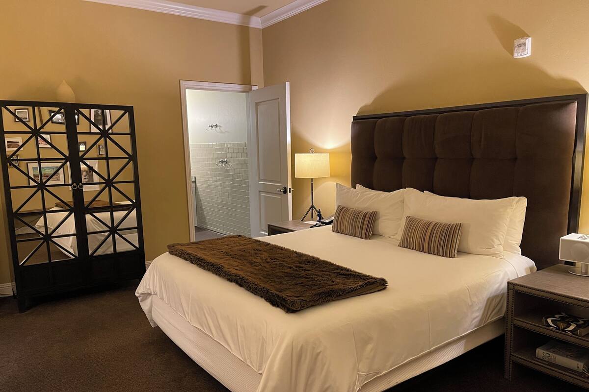 A hotel room with a large bed, a nightstand, a lamp, and a decorative screen.