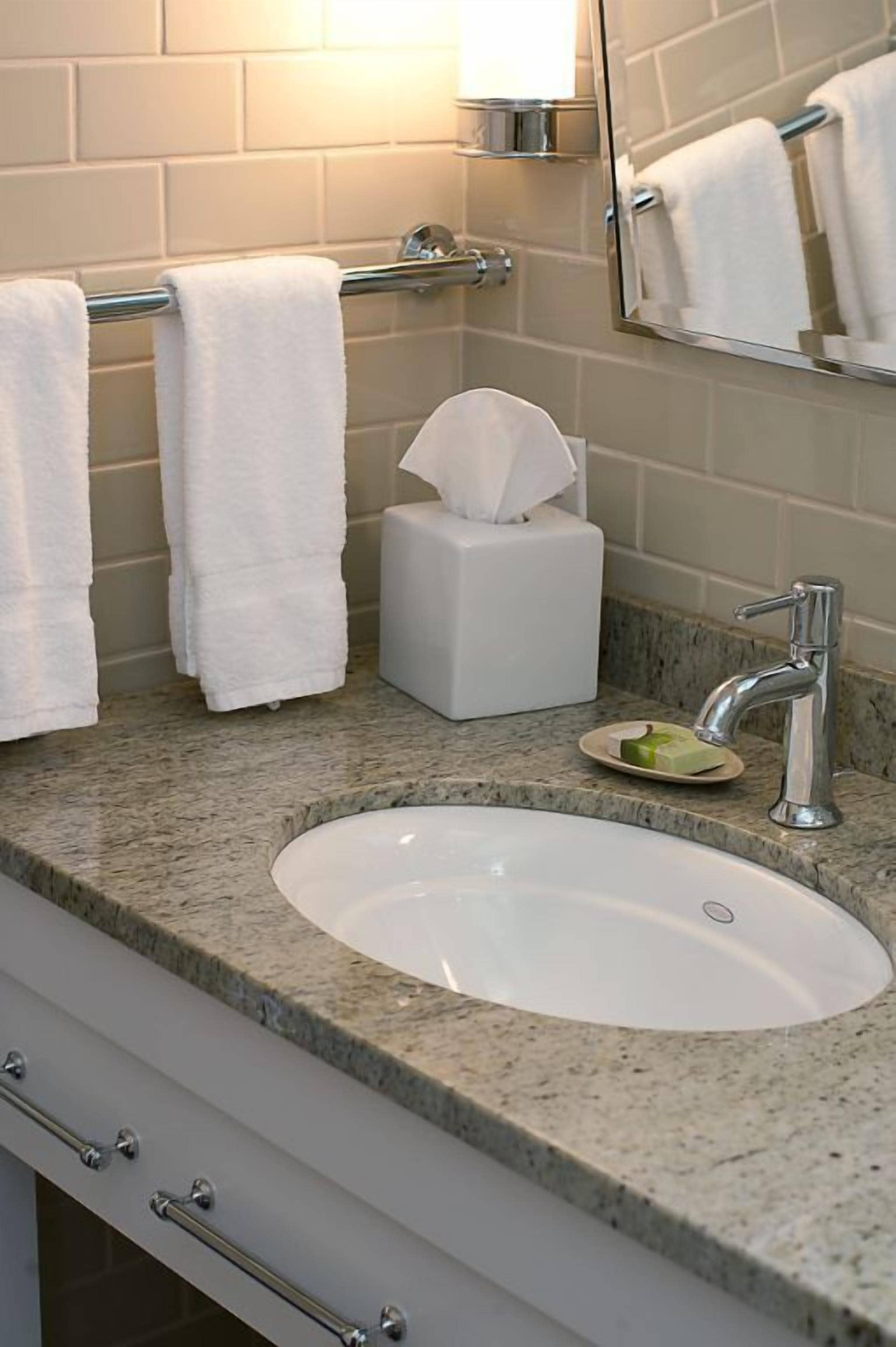 A bathroom with a white sink, a towel rack with white towels, a tissue box, and a mirror.