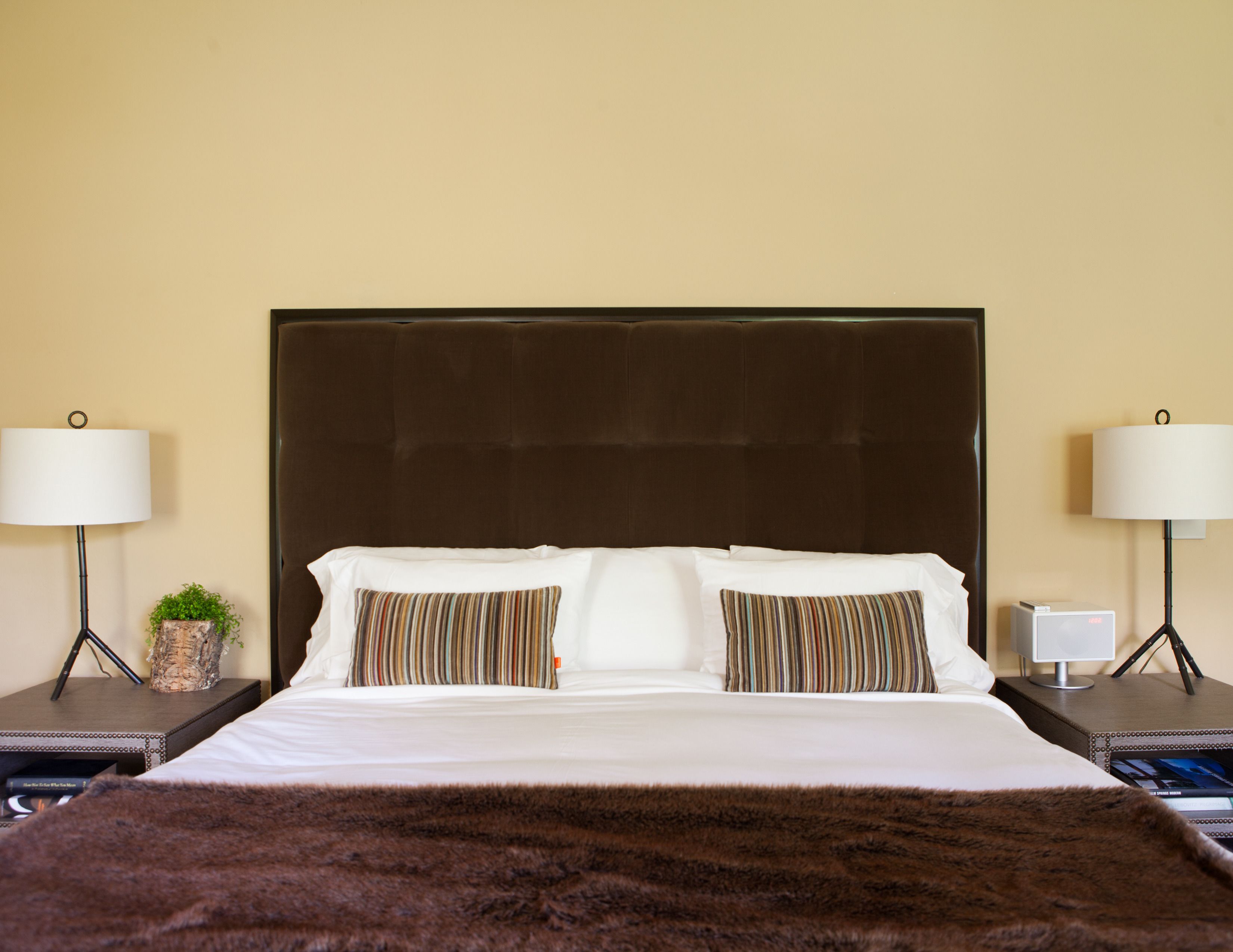 Une chambre d’hôtel avec un grand lit, deux tables de chevet, une petite table d’appoint, une lampe et une petite plante.