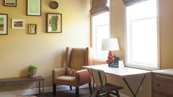 Una habitación con escritorio, silla y cama. Hay cuadros en la pared, una lámpara en el escritorio y una ventana con persianas.