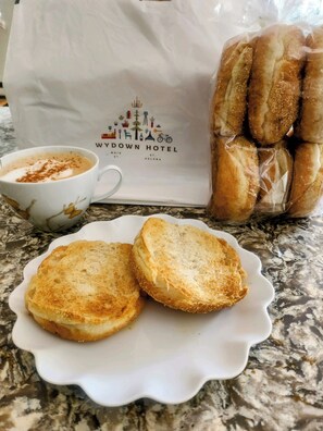 A cup of coffee with a sprinkle of cinnamon, a plate with two pieces of toasted bread, and a bag of bread rolls. - Wydown Hotel (St. Helena)