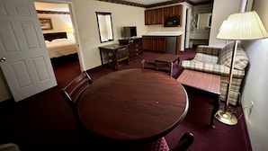 Una habitación de hotel compacta con una mesa de comedor, un sofá, un televisor y una kitchenette.