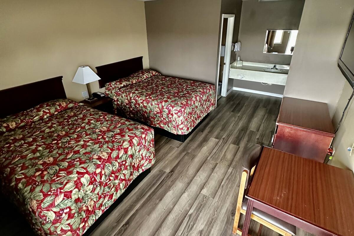 A hotel room with two beds, a wooden floor, a small desk, and a mirror.