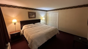 Una habitación de hotel con cama, dos lámparas de noche, una mesita de noche, un cuadro en la pared y una puerta.