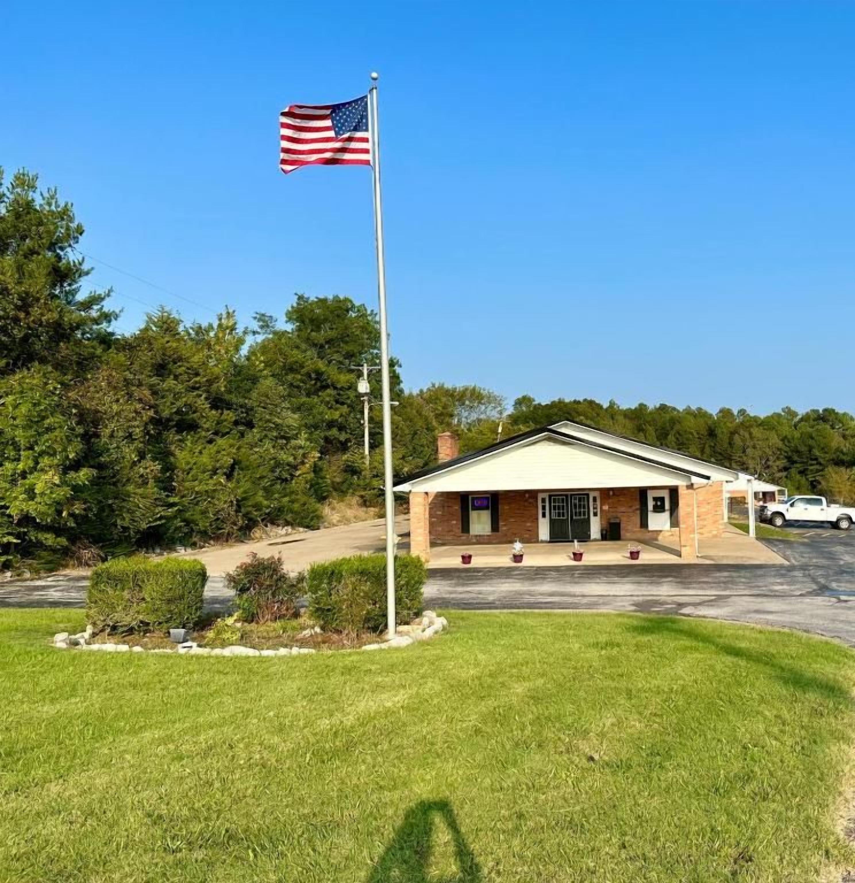 A building with a flagpole, a parking lot, and a grassy area.