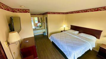 Una habitación de hotel con una cama, un escritorio, un espejo, una lámpara y vista a otra habitación.