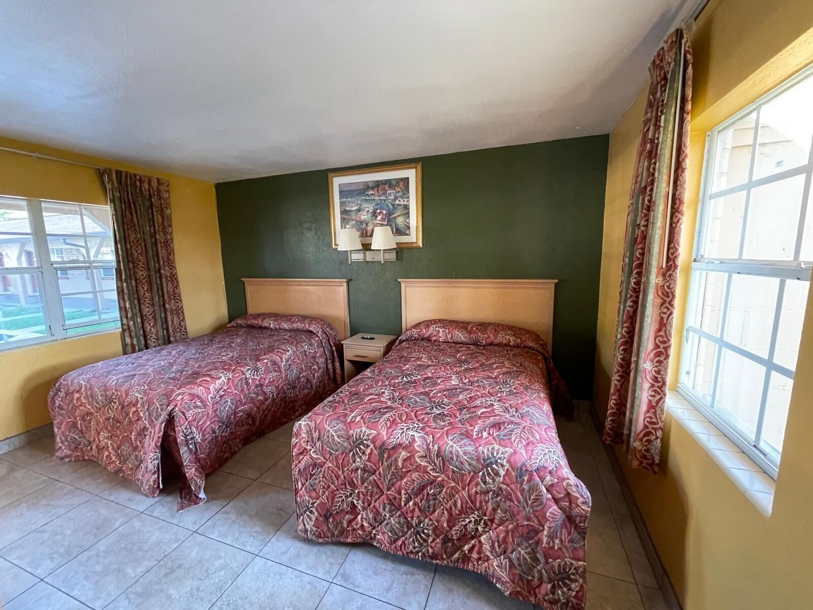 A room with two beds, a painting on the wall, and a window with curtains.