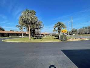 A motel with a parking lot, a covered outdoor seating area, and a sign for the Shangri-La Motel. - Shangri La Motel  (Ocala)