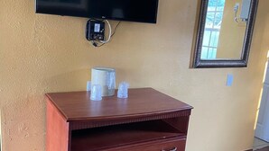 A room with a wooden dresser, a flat-screen TV, a mirror, and a wall socket.