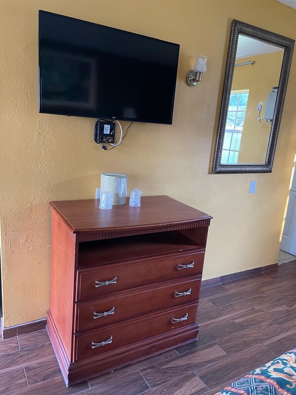 Une chambre avec une commode en bois, un téléviseur à écran plat, un miroir et une prise électrique au mur.