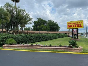 A motel with a signboard, a lawn, and a building with a porch. - Shangri La Motel  (Ocala)