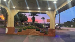 A gas station with a covered area, a palm tree, and a sunset in the background. - Shangri La Motel  (Ocala)