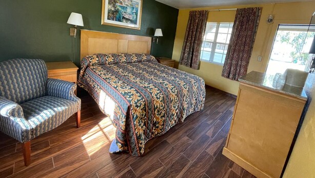 A room with a bed, a chair, a painting on the wall, and a window with curtains.