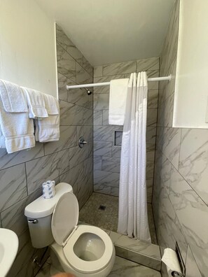 A small, modern bathroom with a shower, toilet, and sink, all with marble tiles. - Shangri La Motel  (Ocala)