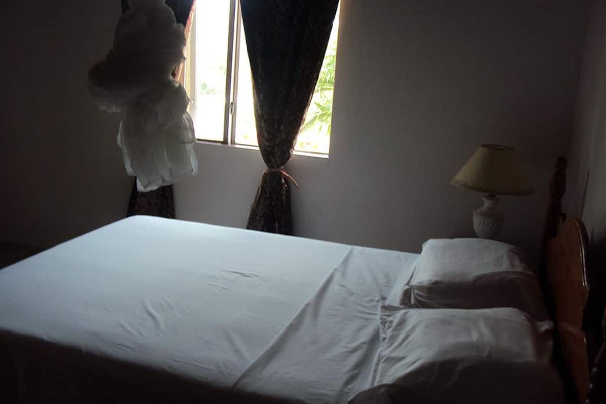 Een gedimd verlichte hotelkamer met een bed, een lamp en een gitaar.