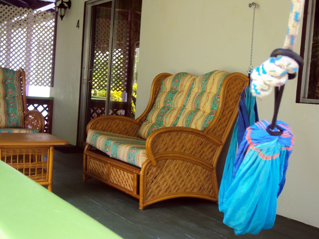 A wicker sofa with a patterned cushion, a hanging blue garment, and a wooden table in a room with a lattice window and a door.