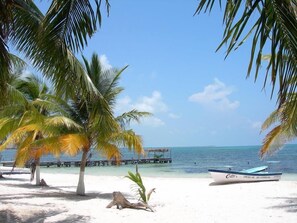 A beach with palm trees, a boat, and a pier extending into the water. - Friendship Garden Apartments (Bequia Island)