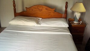 A neatly made bed with a wooden headboard, a bedside lamp, and a nightstand with a telephone.
