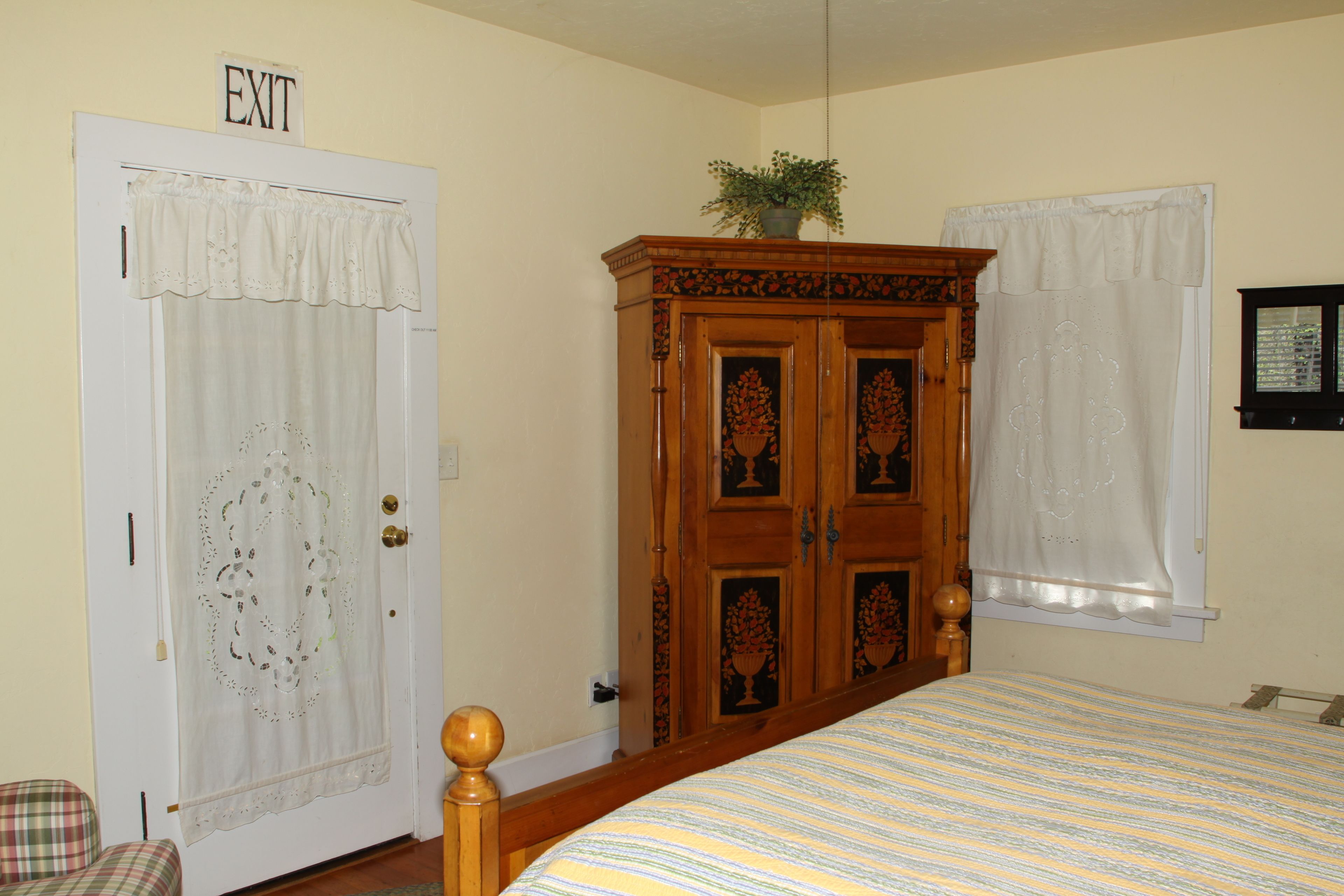 Un dormitorio con cama, armario, puerta con letrero de 'SALIDA' y ventana con cortina.