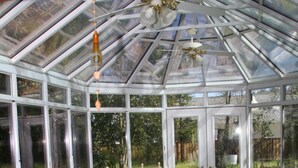 A conservatory with a glass ceiling, a table with a green tablecloth, wooden chairs, and a potted plant. - Bear Flag Inn (Calistoga)