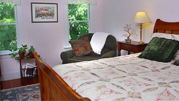 A bedroom with a bed, a chair, a nightstand, a lamp, and a window with a view of greenery.