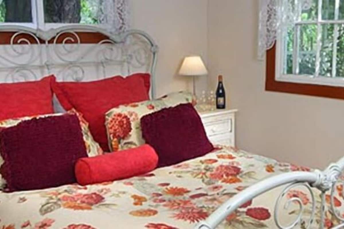 Une chambre à coucher avec une couvre-lit à motifs floraux, un cadre de lit en métal blanc et une table de chevet sur laquelle se trouvent une lampe et une bouteille.