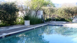A swimming pool with a tiled edge, surrounded by greenery and a building in the background. - Bear Flag Inn (Calistoga)