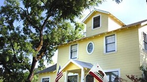 A yellow two-story house with a front porch, an American flag, and a small sign. - Bear Flag Inn (Calistoga)