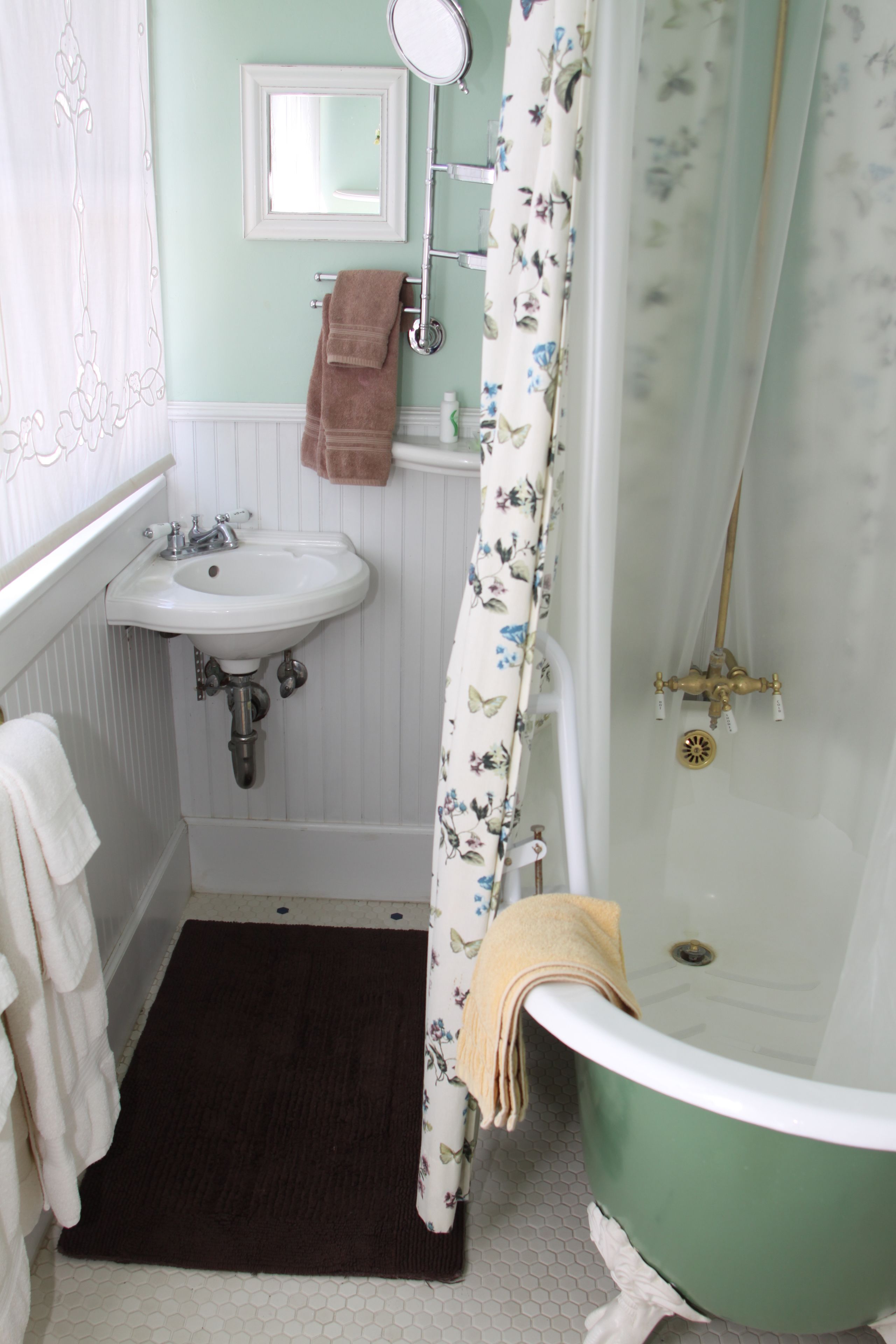 A bathroom with a white sink, a green bathtub, and a white shower curtain with a floral pattern.