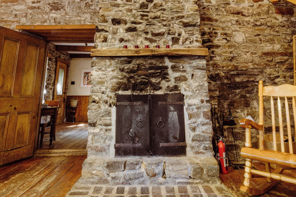 A stone fireplace with a wooden mantel, a wooden staircase, and a wooden rocking chair.