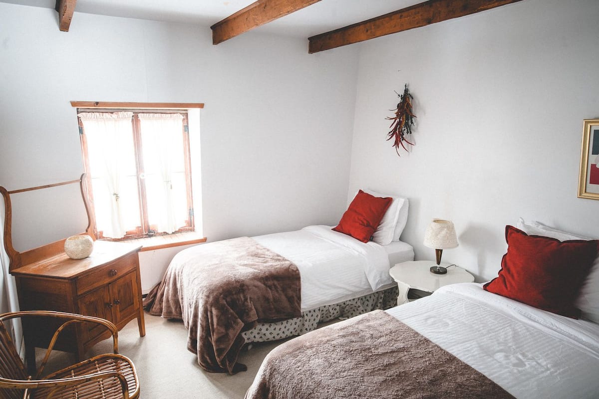 A bedroom with two beds, a wooden dresser, a chair, a lamp, and a window.
