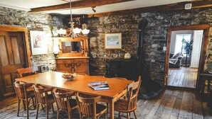 A rustic dining area with a wooden table and chairs, stone walls, and a chandelier. - Le Clos des Brumes (Chateau-Richer)
