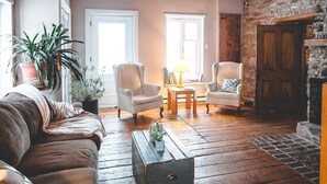 A cozy living room with a wooden floor, two armchairs, a sofa, a coffee table, and a fireplace. - Le Clos des Brumes (Chateau-Richer)