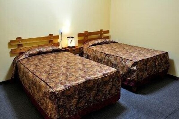 Two single beds with patterned bedding in a room with a wooden headboard and a bedside lamp. - HOSTAL LOS UROS (Puno)