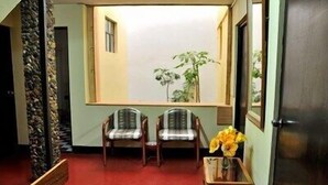 Una habitació amb dues cadires, una taula petita amb un ram de flors i una finestra amb vista a vegetació.