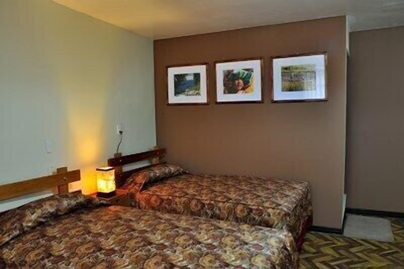 A twin room with two beds, a nightstand, and a wall-mounted lamp.