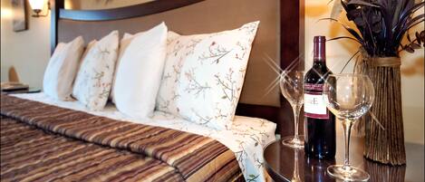 Una cama bien hecha con ropa de cama floral, una botella de vino y dos copas de vino sobre una mesita de noche.
