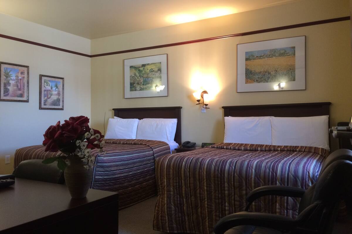 A hotel room with two beds, a desk, a chair, and a vase of flowers.