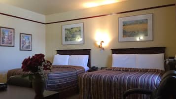 Habitación de hotel con dos camas, un escritorio, una silla y un florero con flores.