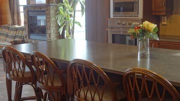 A kitchen with wooden cabinets, a stone fireplace, a large island with chairs, and a vase with flowers.