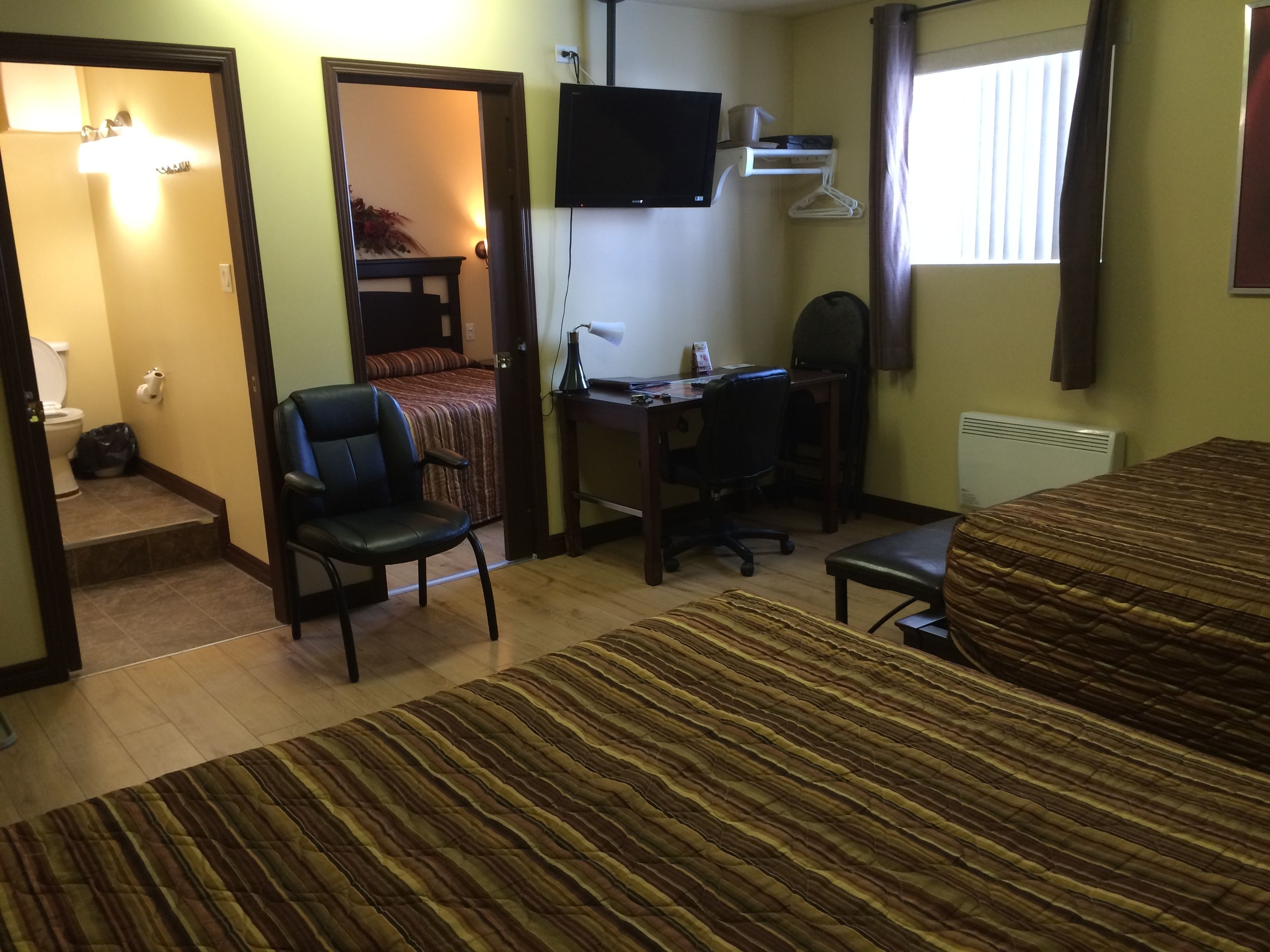 A hotel room with a bed, a desk with a chair, a television, and a bathroom visible through an open door.