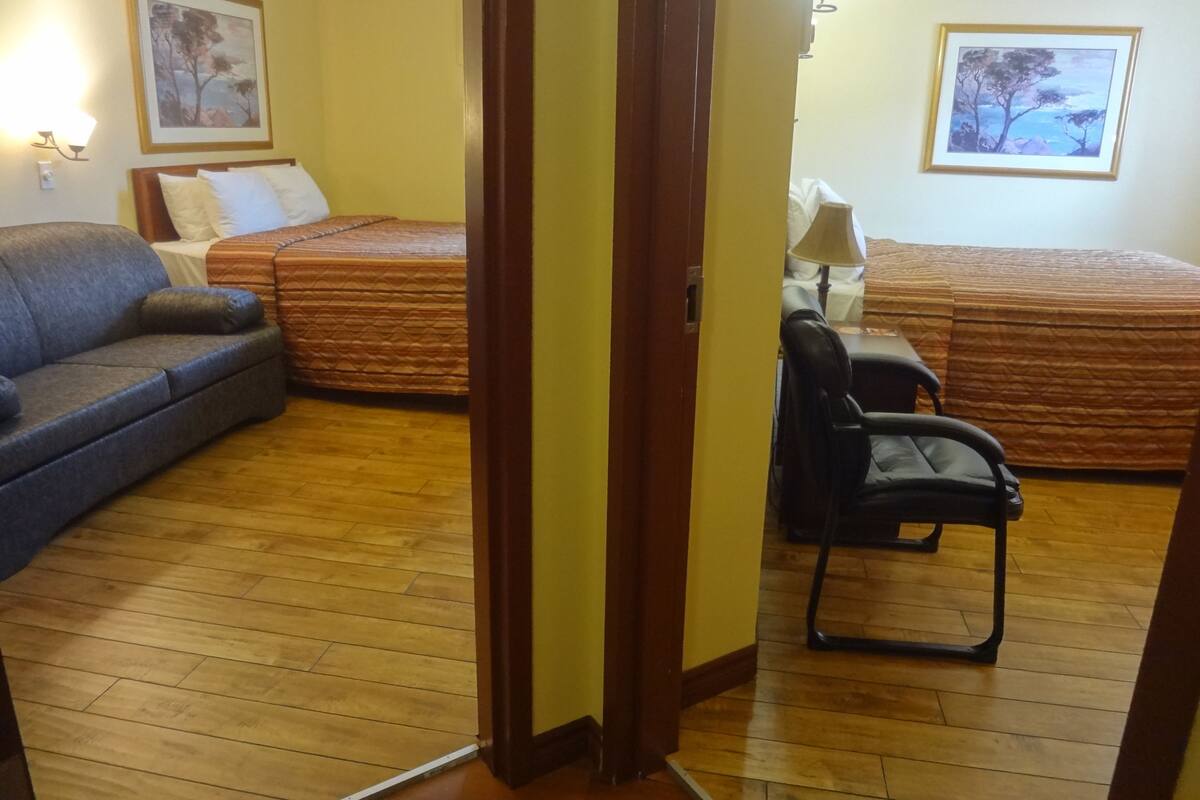 A room with two beds, a sofa, a chair, and two wall-mounted lamps.