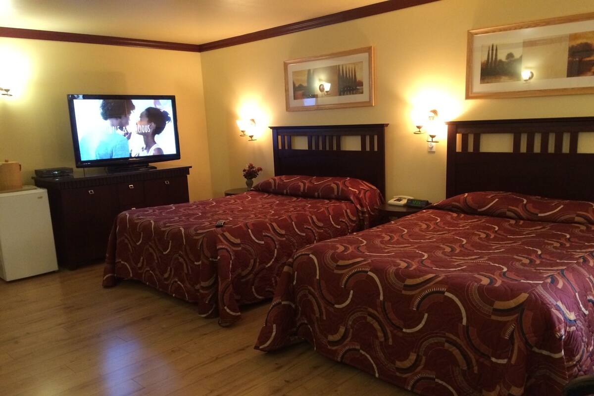 A hotel room with two beds, a television, a small refrigerator, and a nightstand with a lamp.